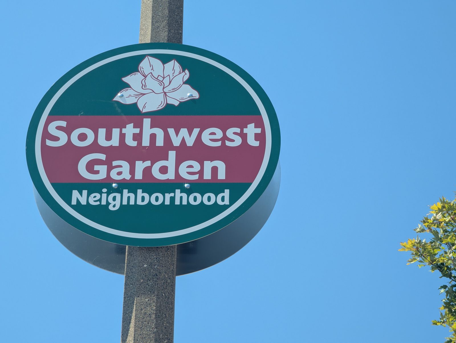 The round green and maroon Southwest Garden Neighborhood sign in south St. Louis, with a magnolia blossom above the name