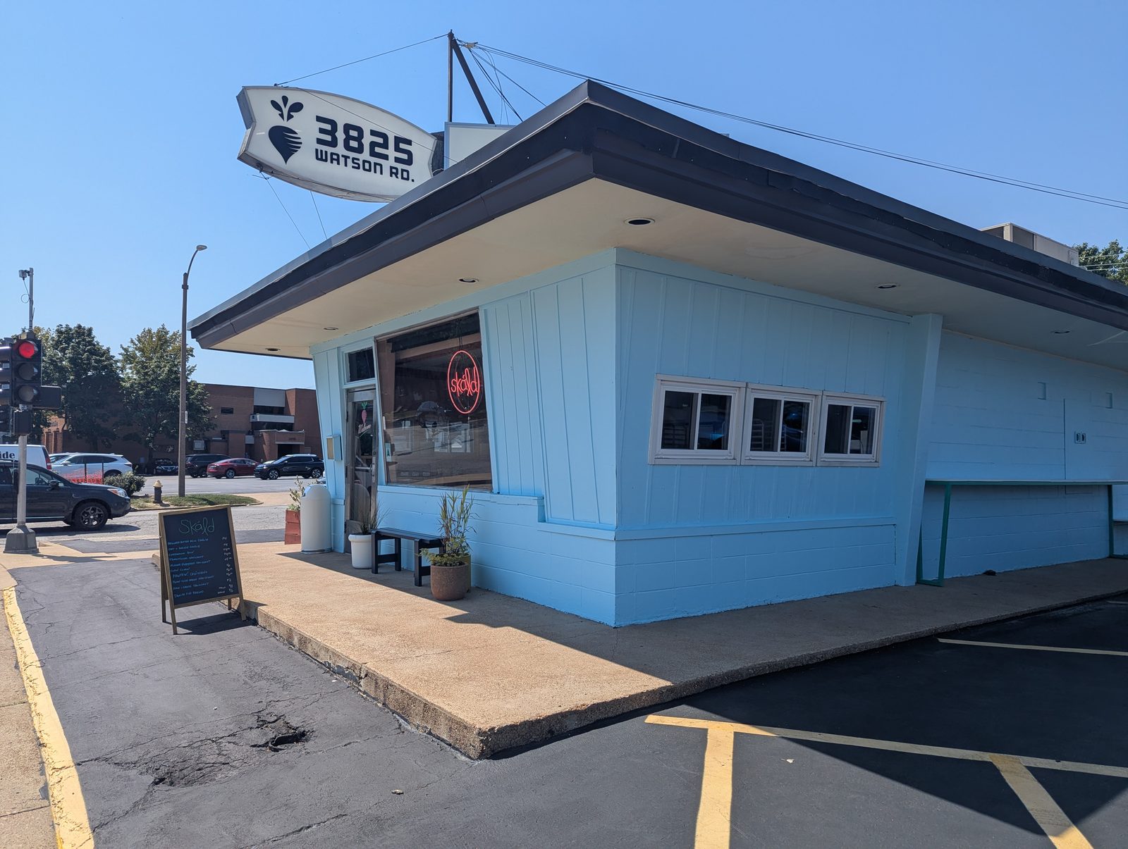 A pale blue mid-century corner building on Watson Road in St. Louis with a chalkboard menu on the sidewalk