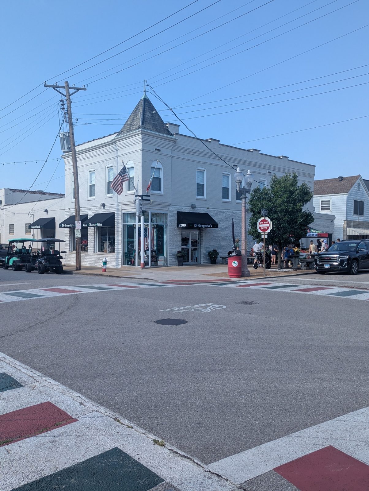 A white turreted corner grocery and import market on Daggett Avenue on The Hill in St. Louis, with the crosswalk painted in Italian tricolor blocks