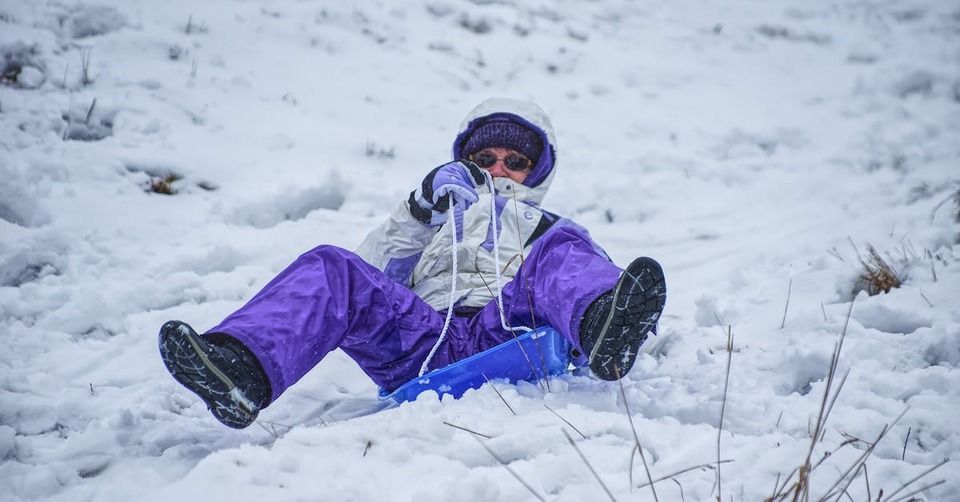 person wearing a blue winter suit sledding down a hill
