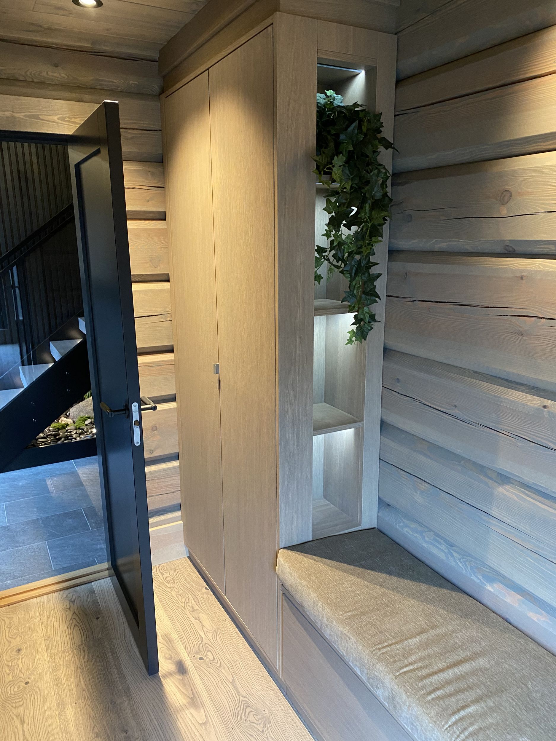 Plassbygget entréskap i lyst treverk med sittebenk og belyste åpne hyller.