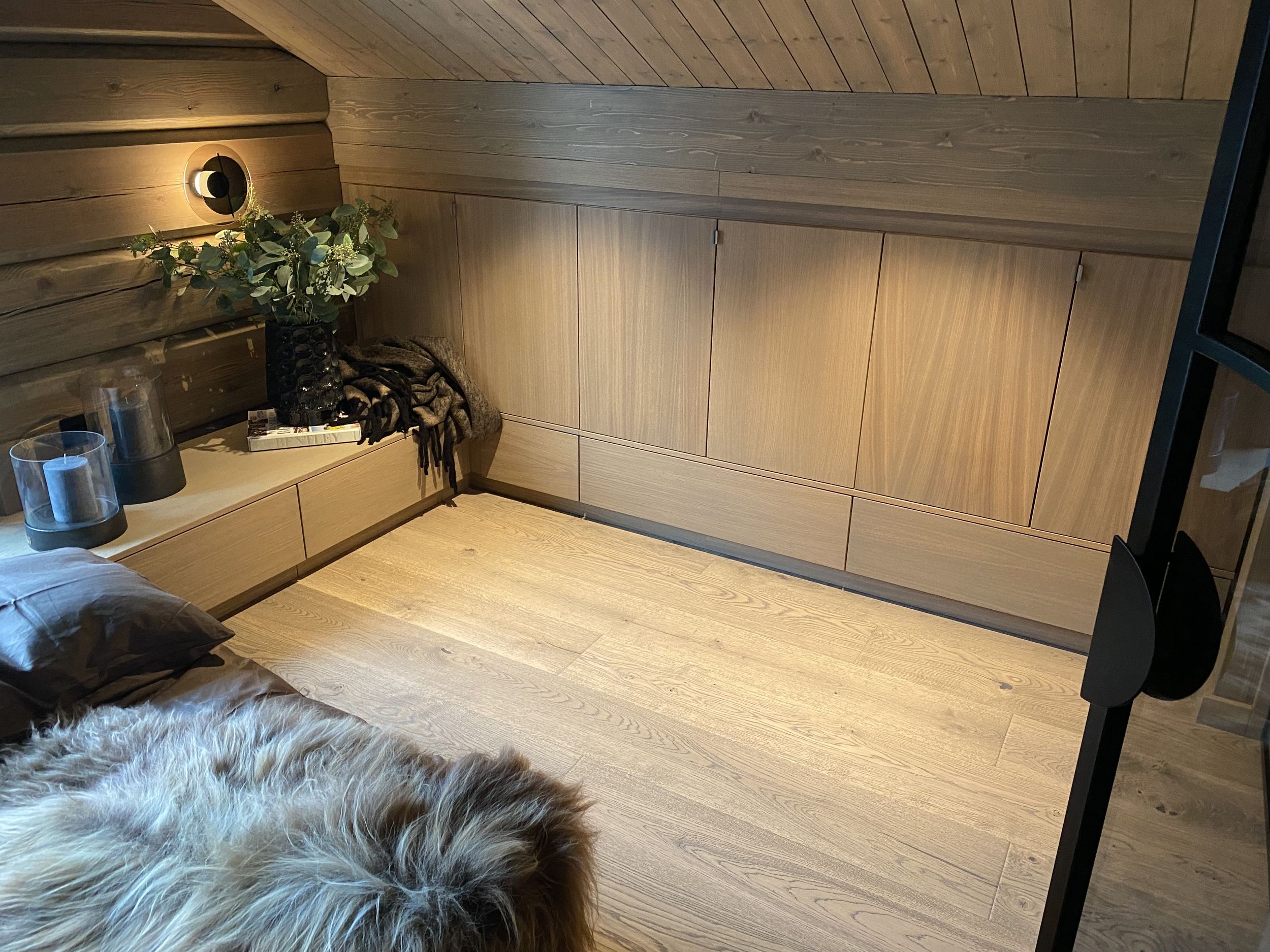 Plassbygget garderobe under skråtak med lave skuffer og sittebenk i soverom.