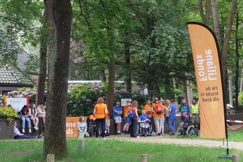 Deelnemers verzamelen bij een pauze plaats van De Koninklijke Loop in Apeldoorn, inclusief rolstoelgebruikers en begeleiders
