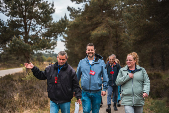 Vier deelnemers wandelen samen over een pad langs heide en bomen.