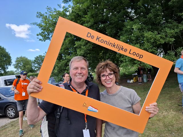Twee mensen met medailles staan samen in een oranje fotolijst van De Koninklijke Loop.