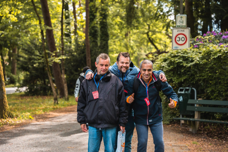 Drie deelnemers staan naast elkaar op een pad, met armen om elkaars schouders.