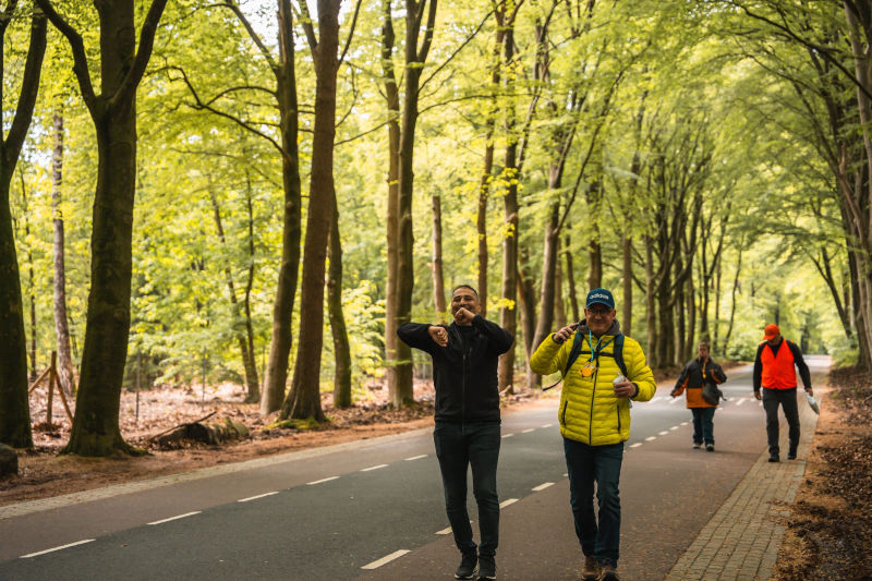 Vier deelnemers wandelen samen over een brede bosweg.