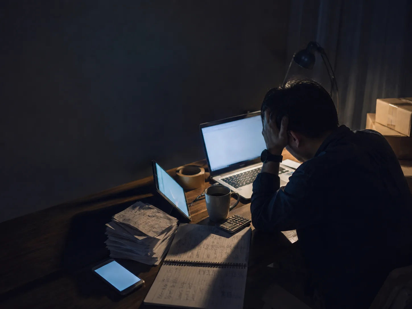 A seller’s desk late in the evening, covered in a laptop, phone, printed orders and handwritten stock notes
