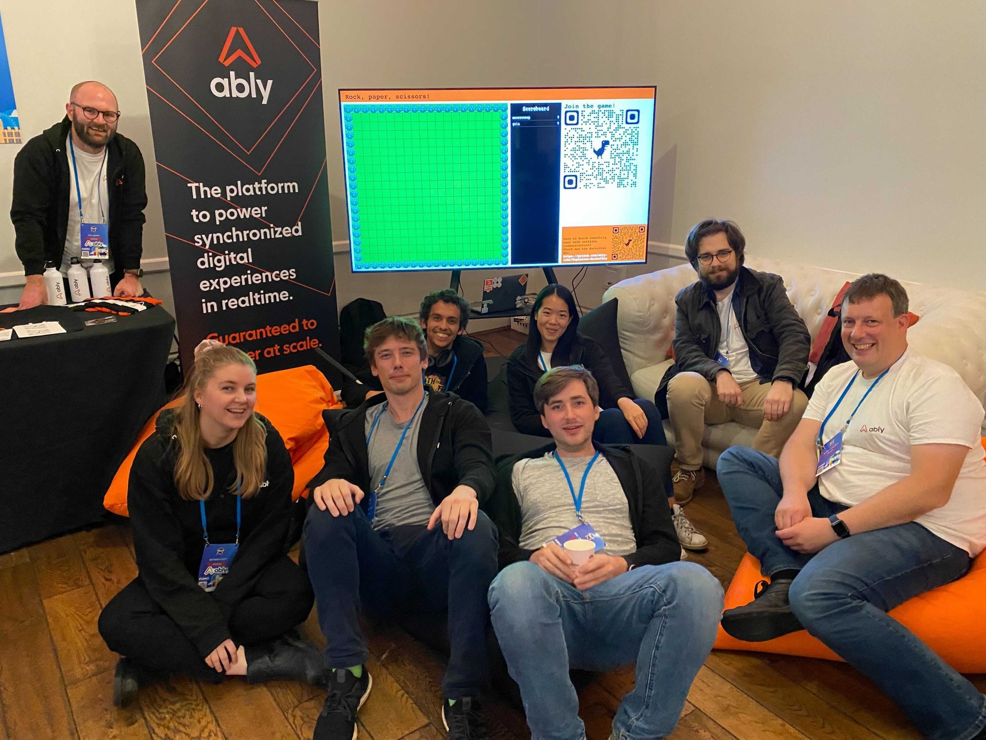 The Ably team sat on bean bags with an Ably banner in the background.
