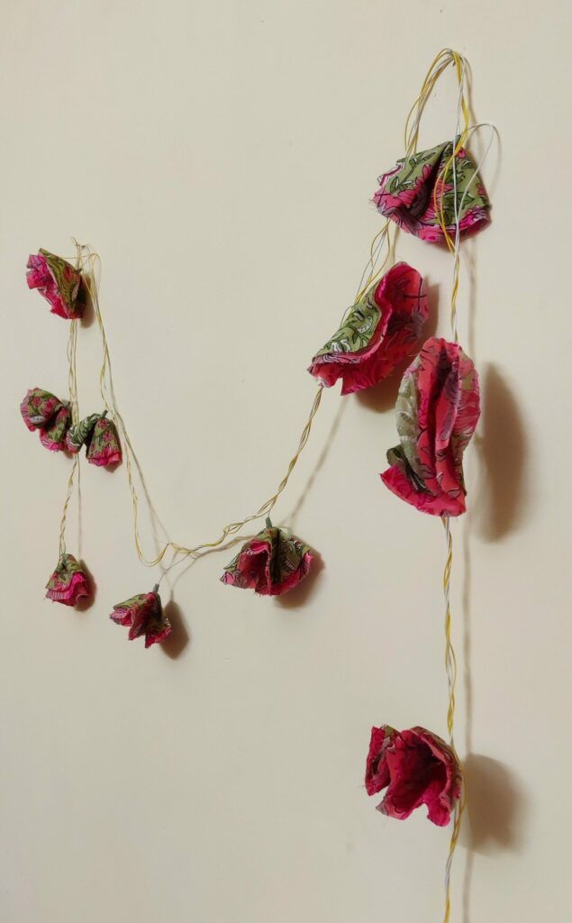 Pink and green fabric flower fairy lights hanging against a cream wall