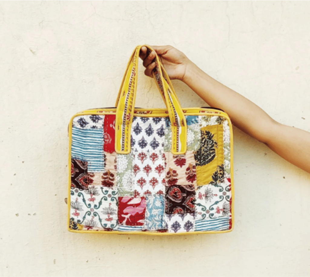 Colourful patchwork laptop bag with yellow handles and trim held against a cream wall