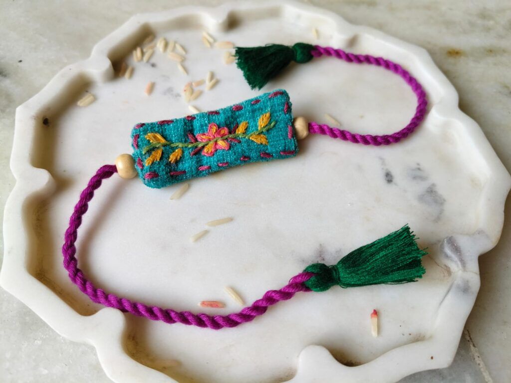Turquoise Flower Embroidery Rakhi with floral stitching and purple ties