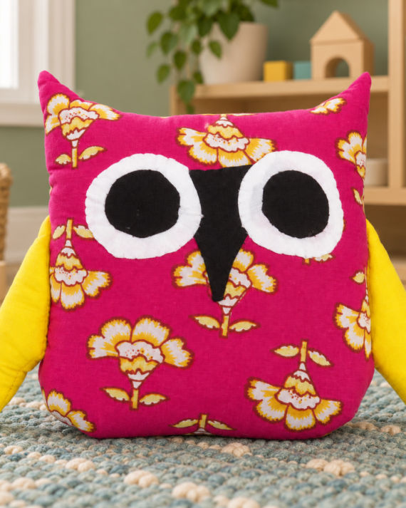 Magenta floral cotton owl toy with yellow wings on a teal play mat in a modern children’s playroom.