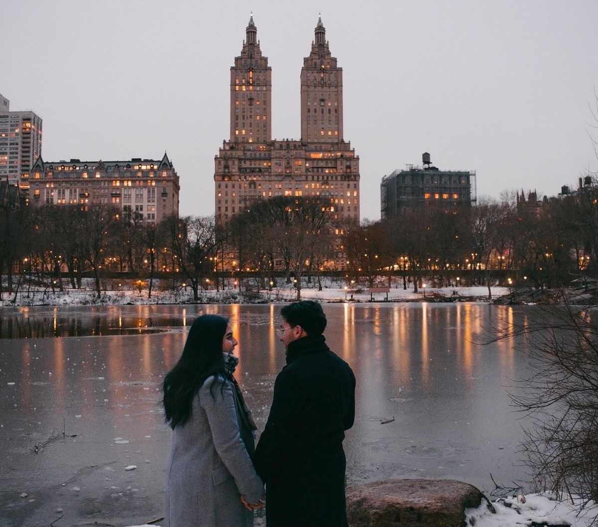 Katia y Salvador tomados de la mano frente al lago helado de Central Park, con las torres iluminadas del San Remo al fondo.