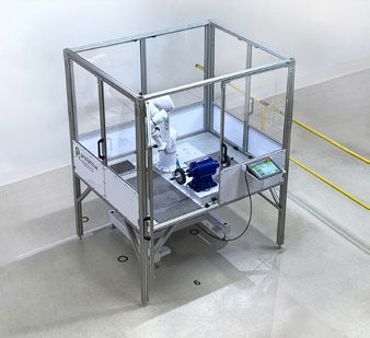 Overhead view of the enclosed deburring cell on the Productive Robotics shop floor. The aluminum-frame enclosure allows the robot to run above collaborative speed limits.