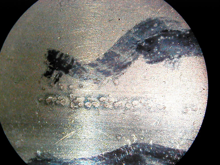 Figure 5—Microscopic view of corrosion pits on a roller bearing raceway, the small round pits between the two heavy black pen marks were caused by corrosion.