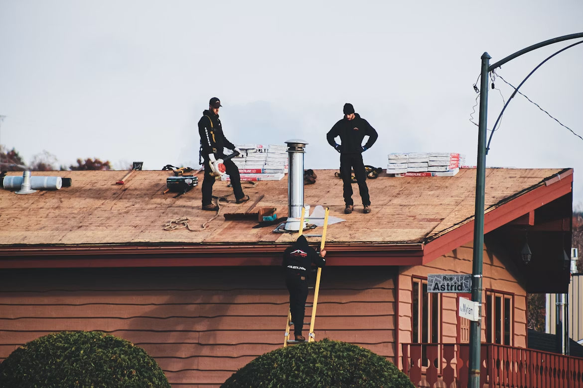 Two construction workers installing roof tiles on a building under a clear blue sky.