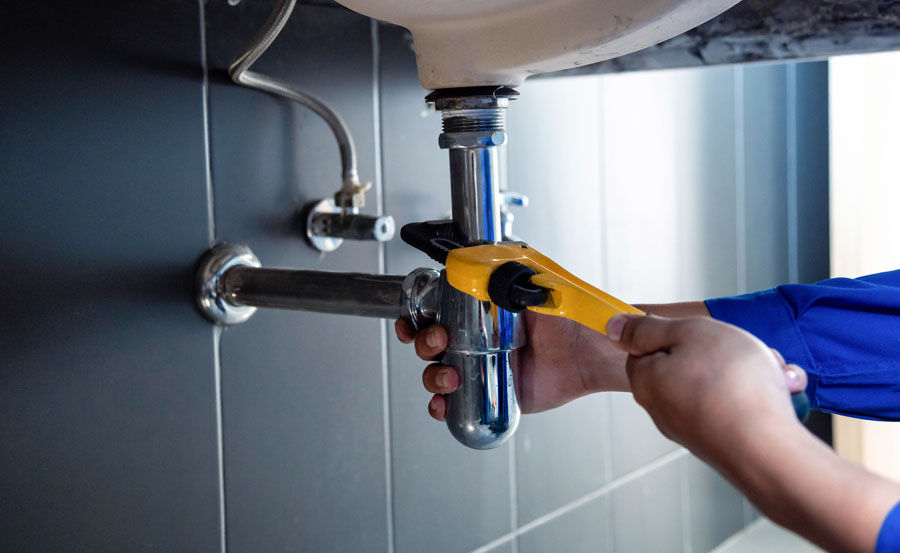 A worker fixing pipes with tools in an industrial indoor environment.