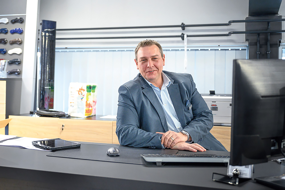Sandro Studerus sitzt am Schreibtisch mit einem blauen Anzug und schaut selbstbewusst in die Kamera