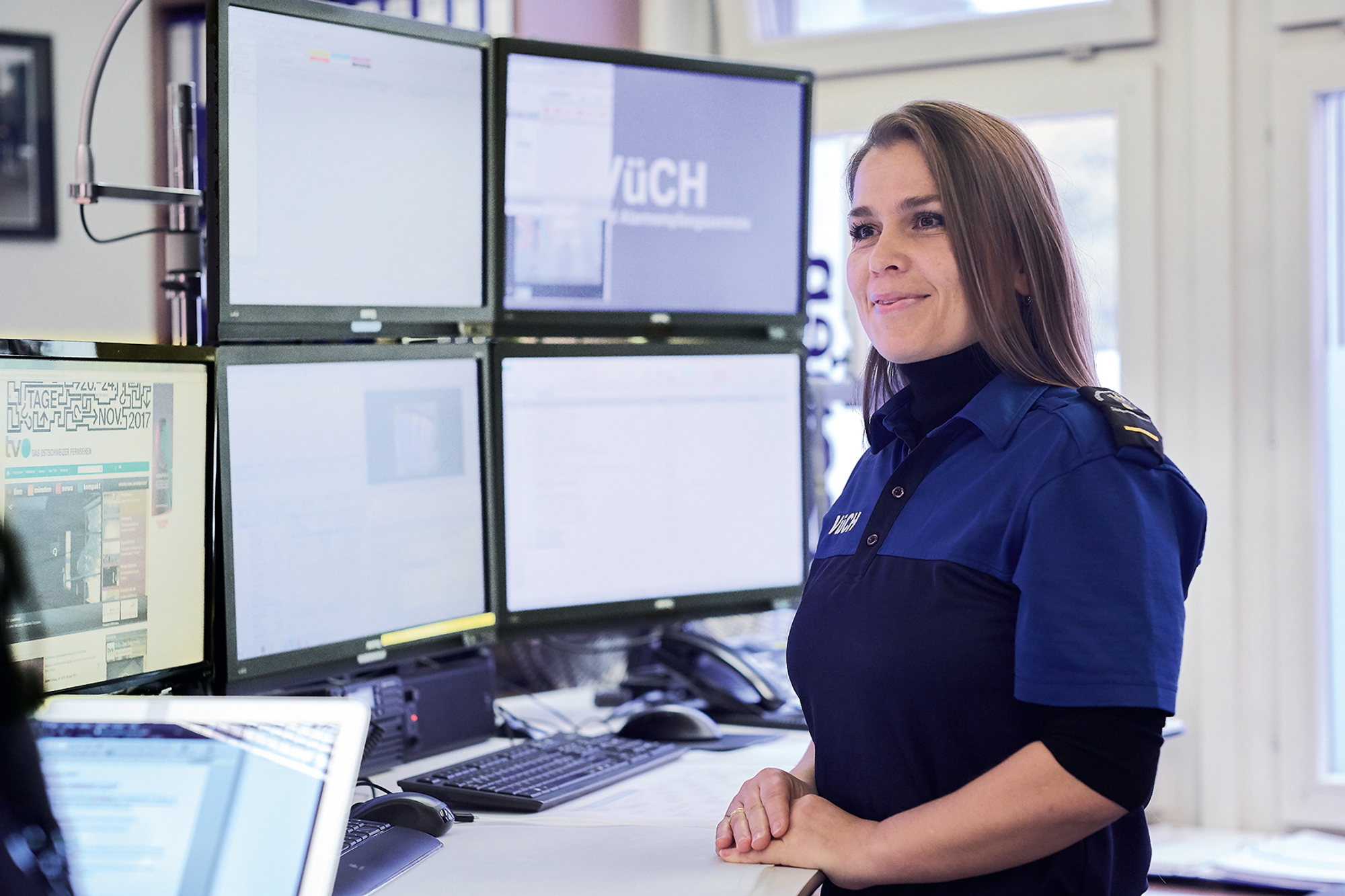 Isamete Asani steht vor Überwachungsbildschirmen des VÜCH