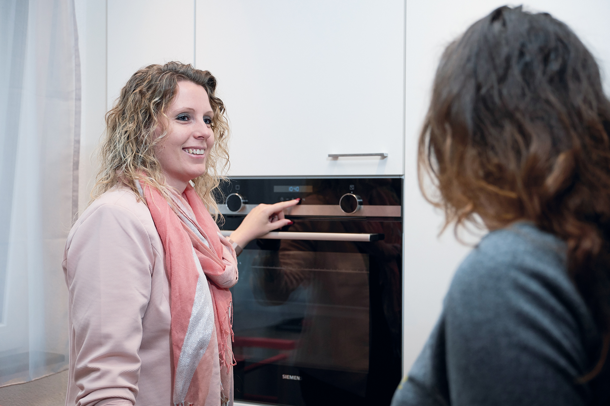 Claudia Strässle steht vor einem Backofen in einer Küche mit einer Kundin