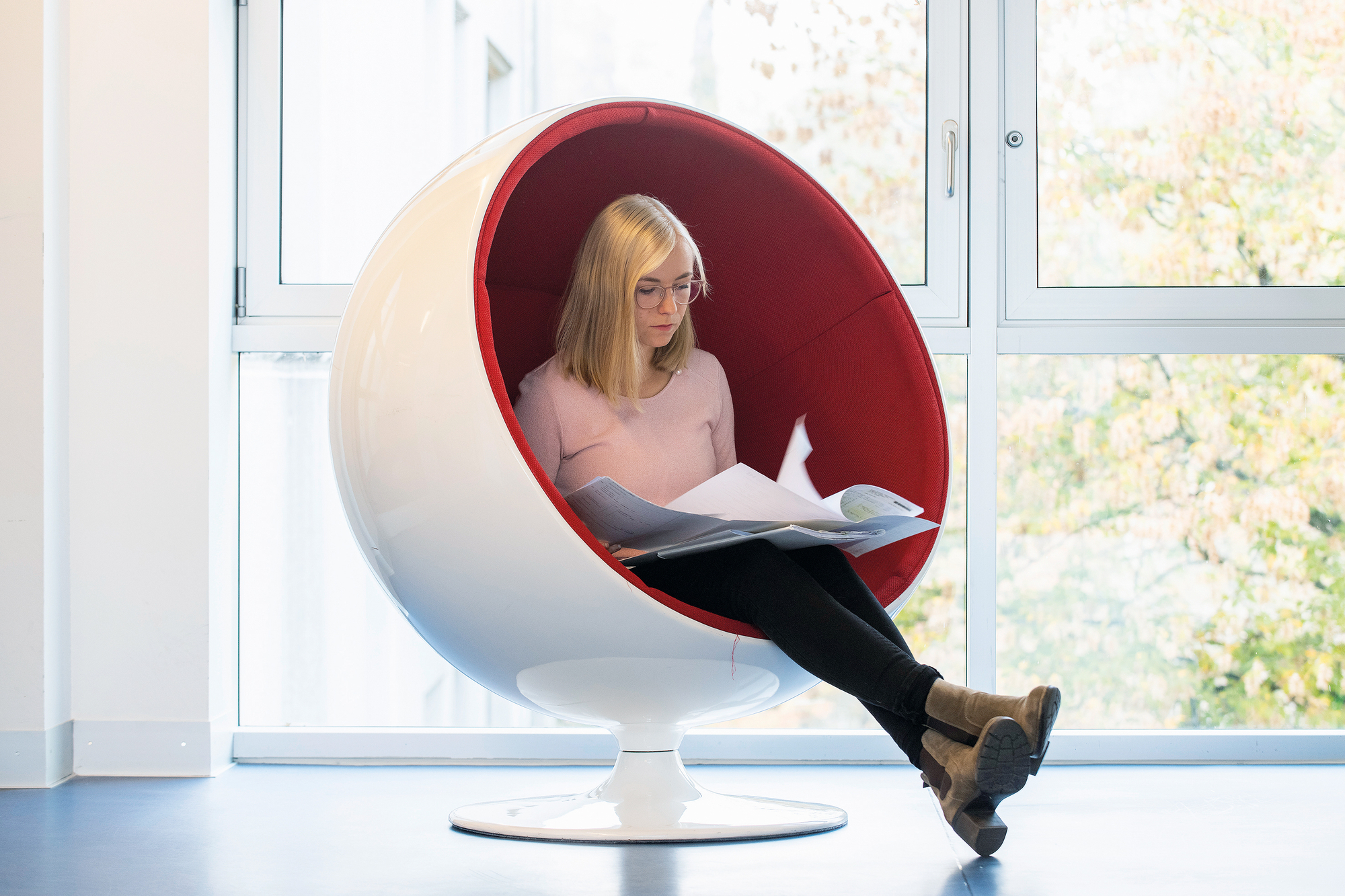 Linda Meier sitzt in einem ovalen roten Stuhl und liest Unterlagen durch Linda Meier sitzt in einem ovalen roten Stuhl und liest Unterlagen durch