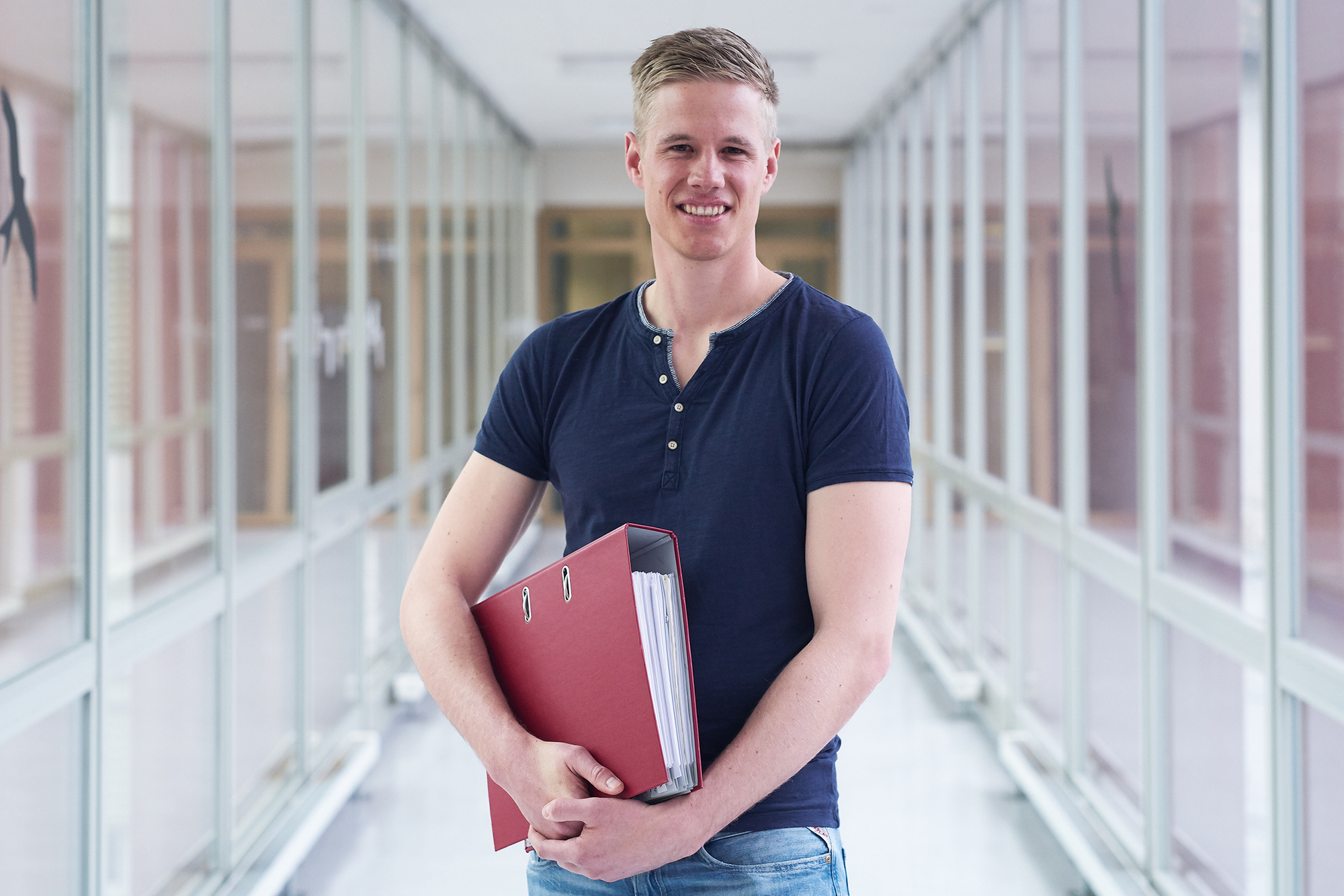 Kevin Scherrer posiert mit einem roten Ordner unter dem Arm