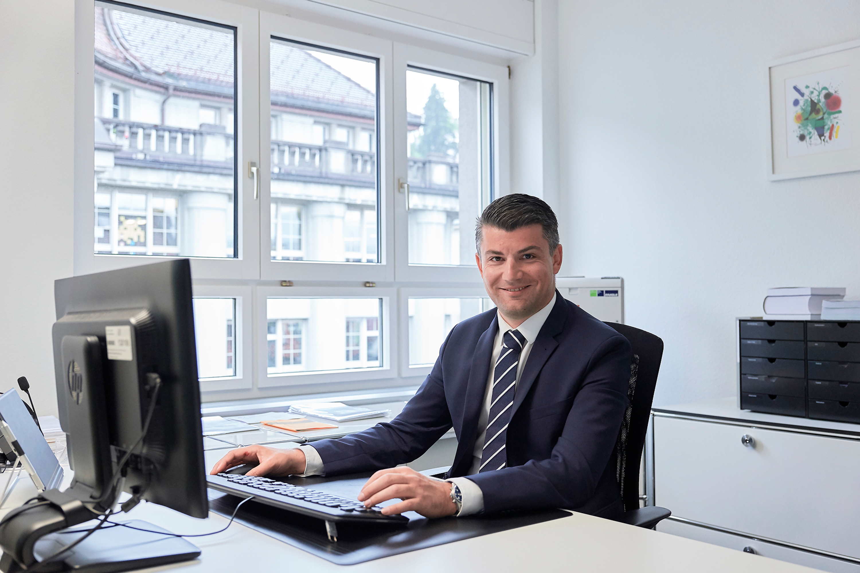 Bogdan Todic an seinem Arbeitsplatz vor dem Bildschirm und lächelt in die Kamera