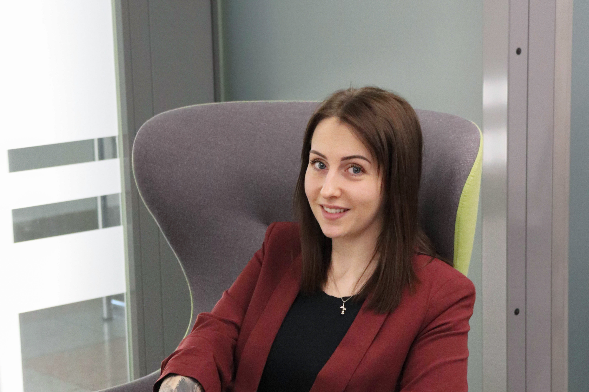 Mischella Kajtez sitzt in einem grüngrauen Stuhl und lächelt in die Kamera
