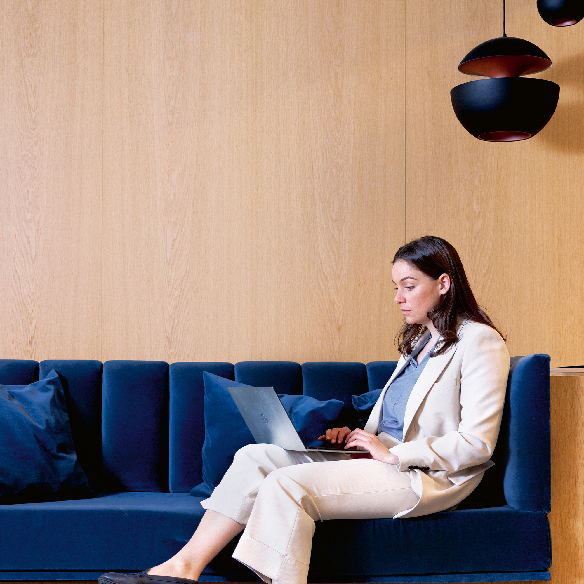 Eine Frau in beigem Anzug arbeitet an ihrem Laptop in der Hotellobby