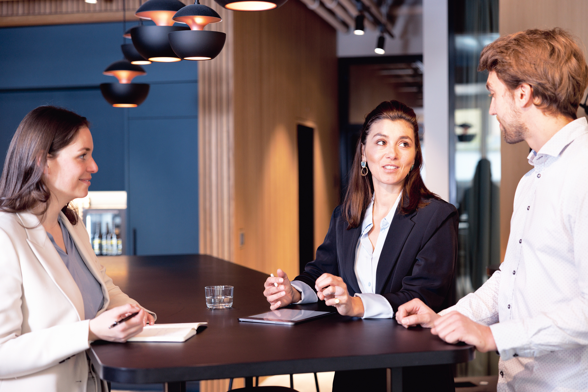 Drei Personen halten ein Meeting an einem Stehtisch.