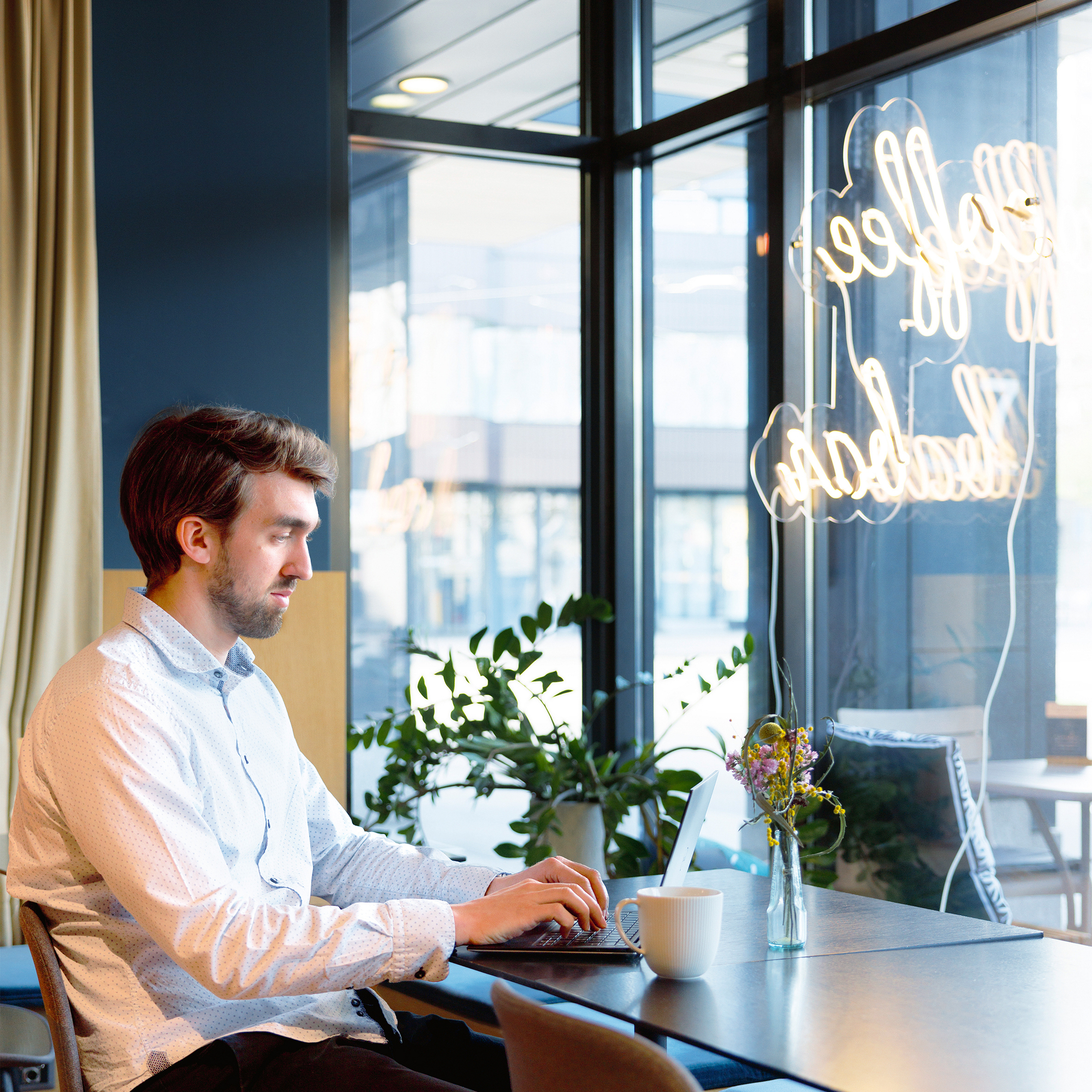 Ein Mann arbeitet in einem Kaffee an seinem Laptop und trinkt eine grosse Tasse Tee