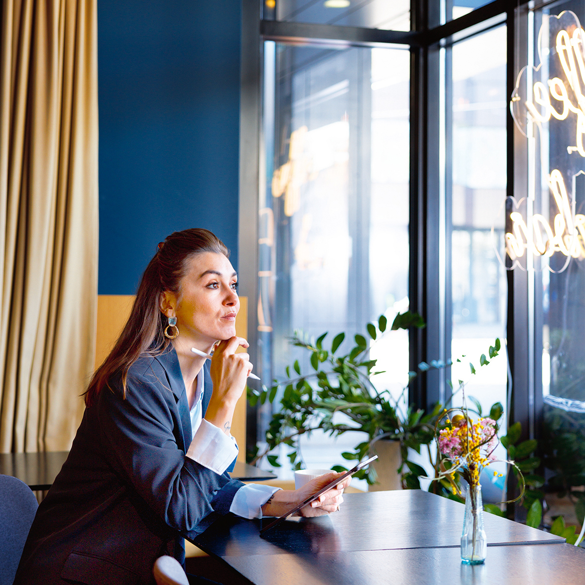 Eine Frau in blauem Anzug sitzt in einem Kaffee und arbeitet an ihrem IPad.