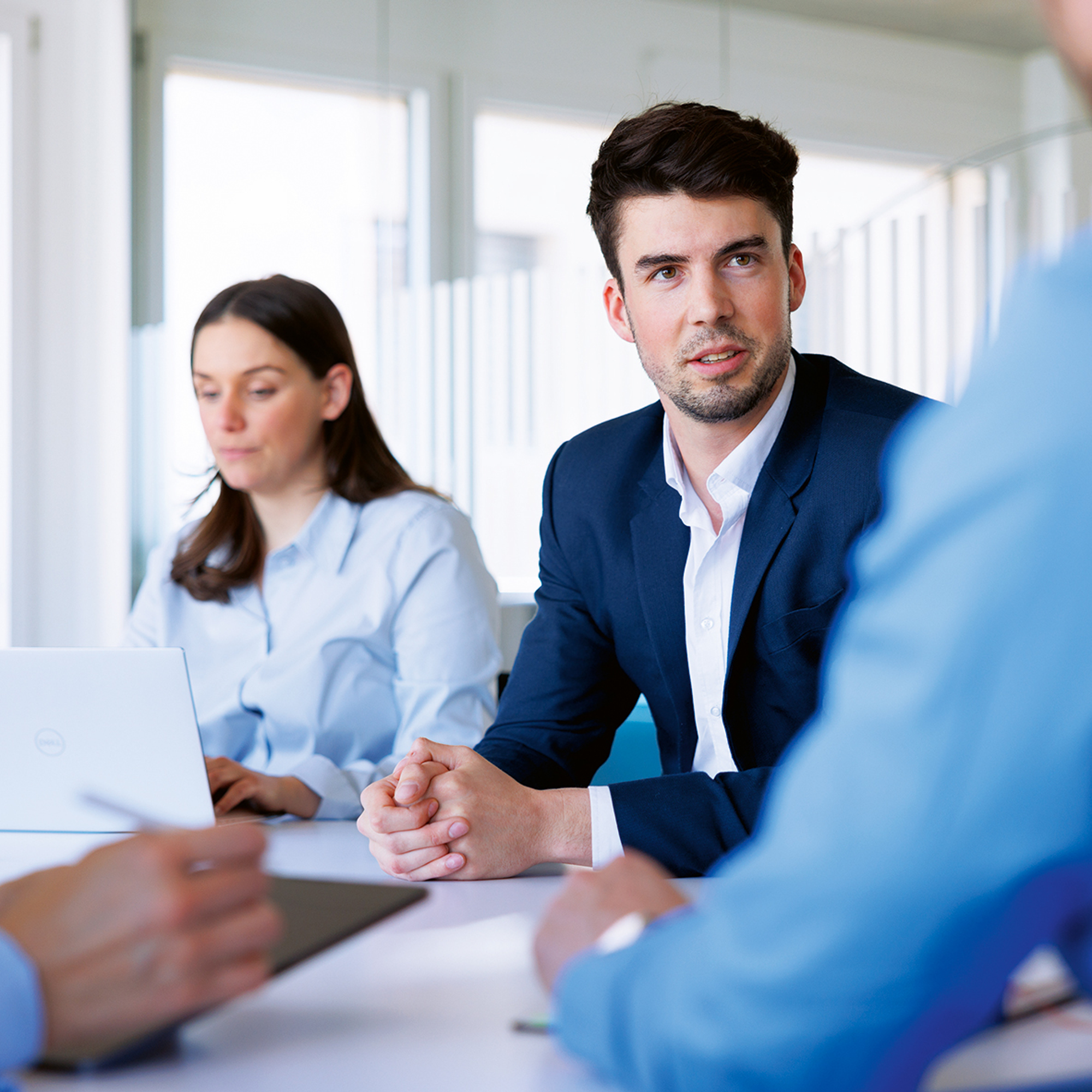 4 Personen in einem Meeting, eine Frau in blauen Hemd macht sich am Laptop Notizen.