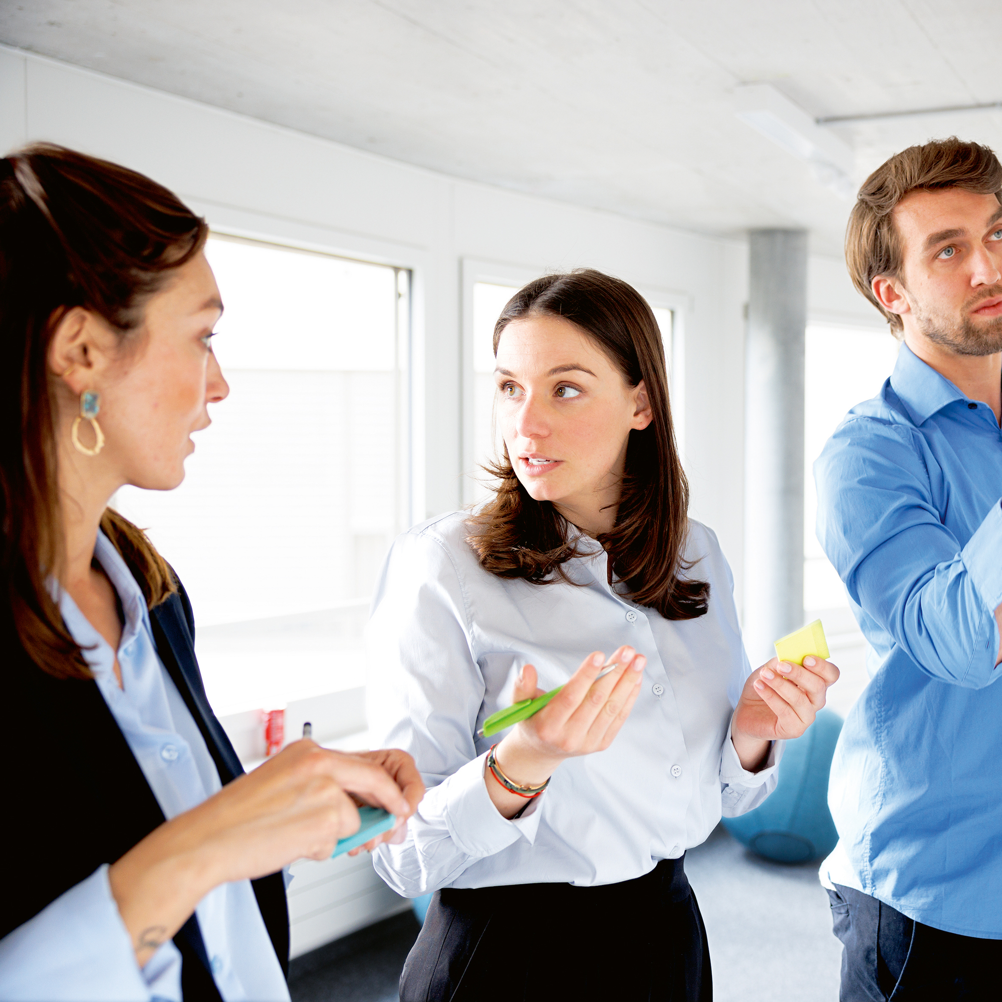 Ein Mann und zwei Frauen halten ein Workshop an einem Whiteboard mit farbigen Post-it.