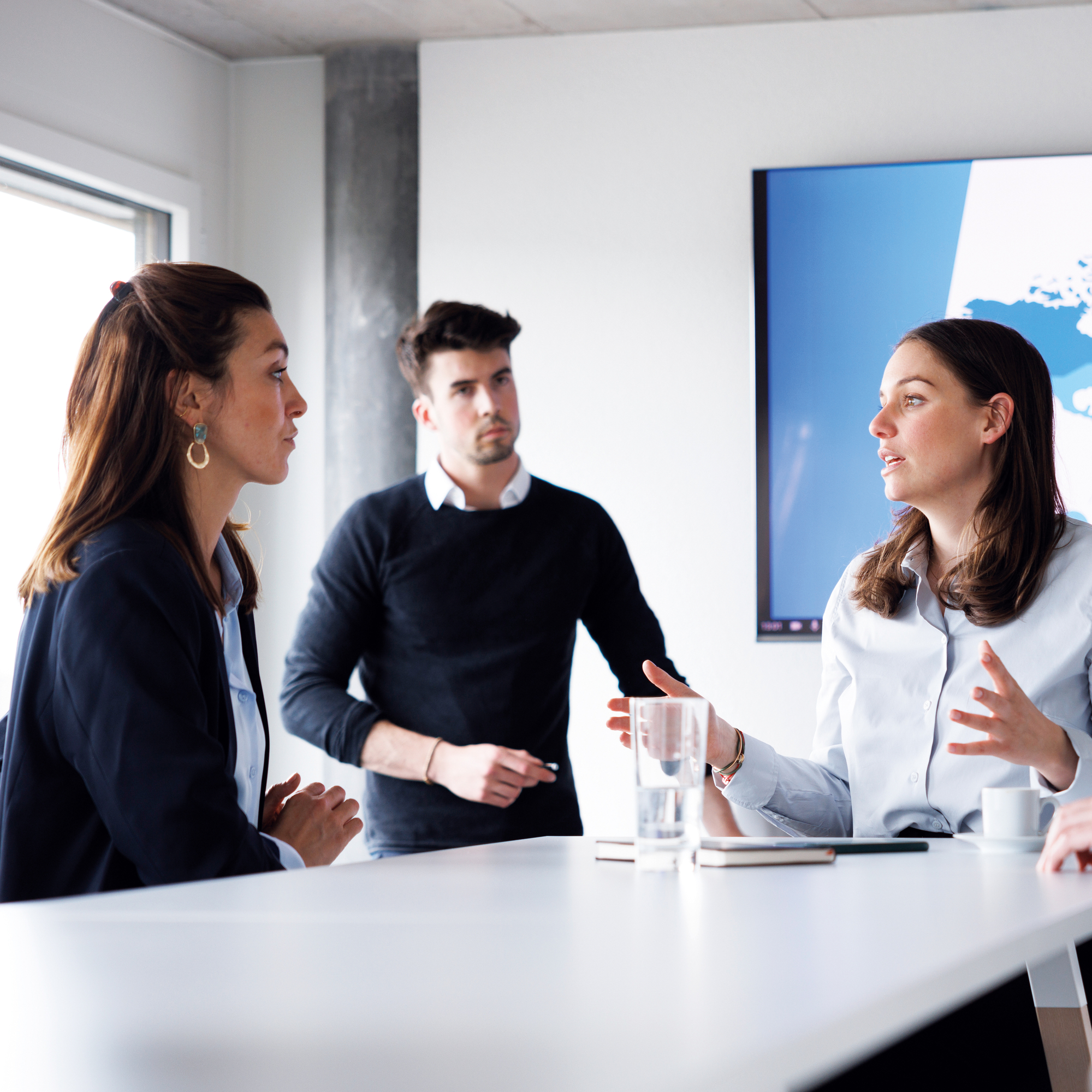 Fünf Personen halten ein Meeting in einem Meetingraum. Zwei Frauen und Zwei Männer, eine Frau ist am sprechen