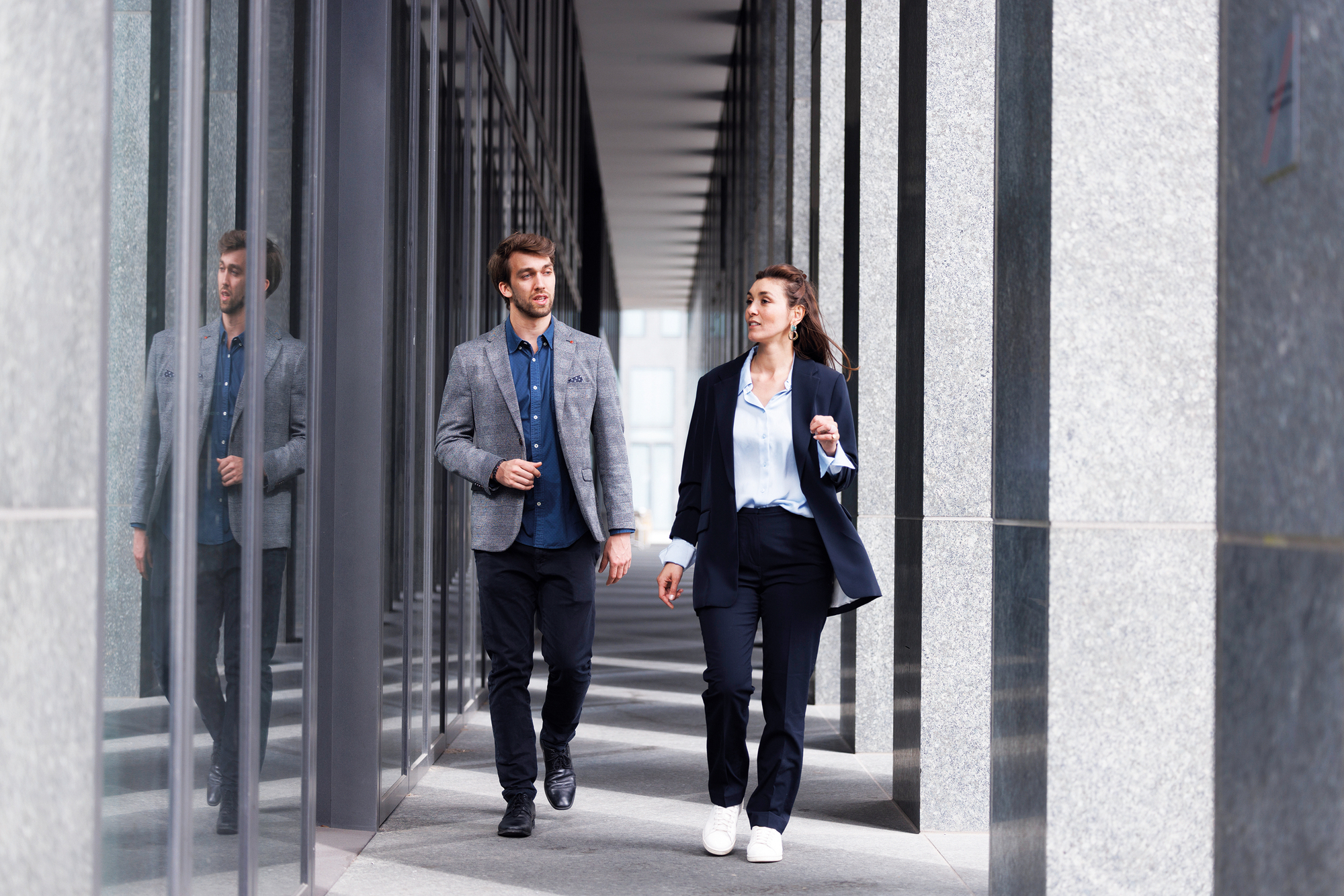 Ein Mann und eine Frau gehen zusammen vor ihrem Unternehmen und unterhalten sich. Beide sind im Anzug.
