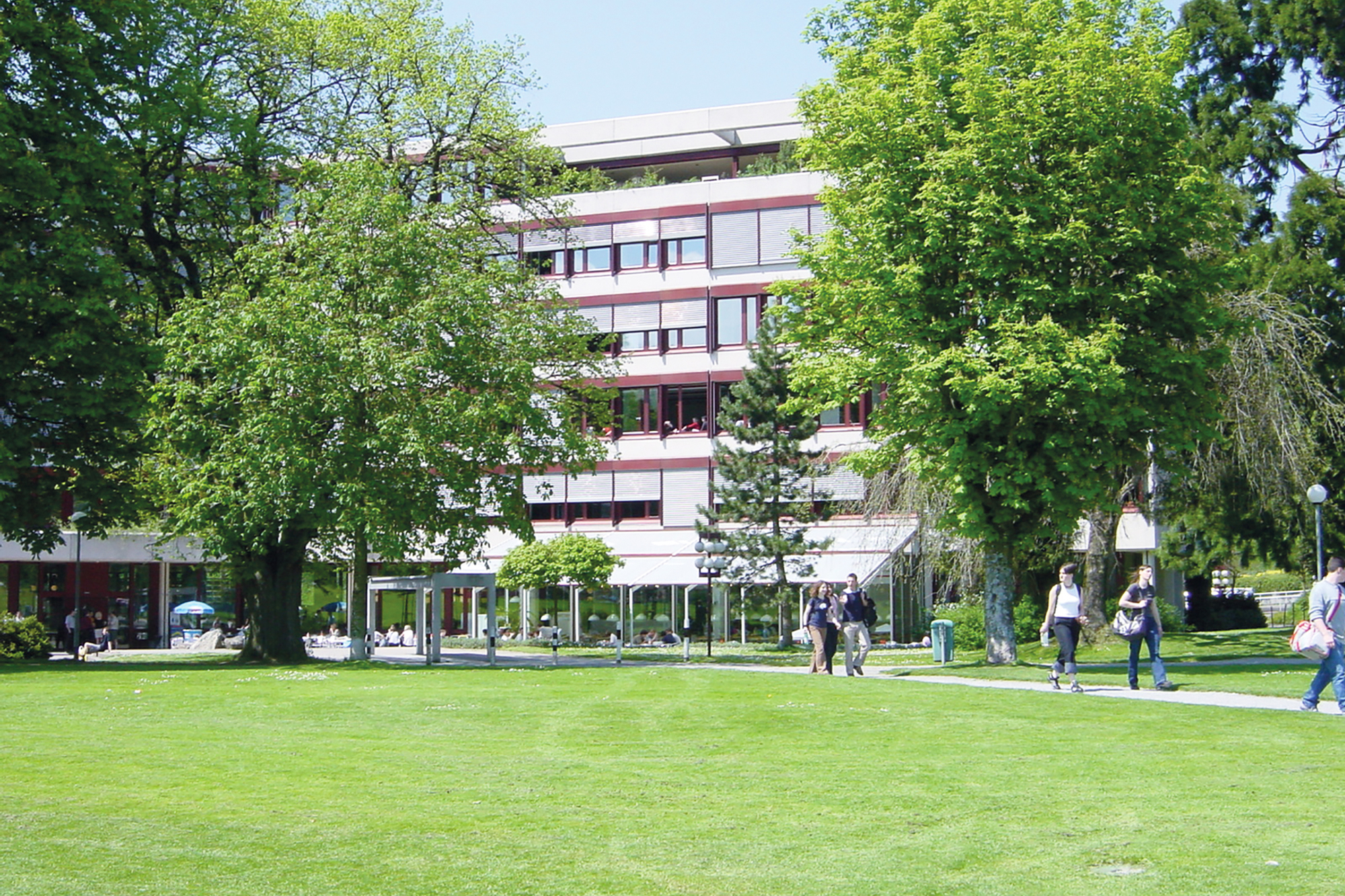 Der Kreuzbleichepark mit dem Gebäude der Akademie St. Gallen im Hintergrund und viele Student:innen welche durch den Park spazieren