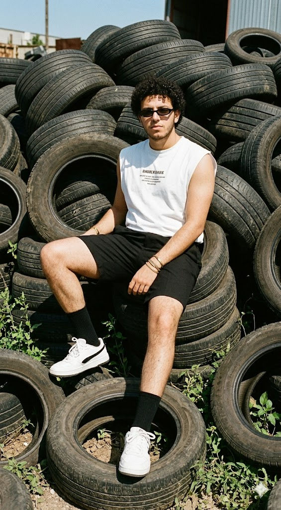 High-Impact Streetwear Fashion Editorial – Young Man on Industrial Tire Stack Outdoor Portrait — 3D AI art prompt example for Midjourney and Stable Diffusion