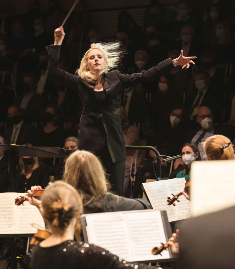 woman directing orchestra inside the concert hall