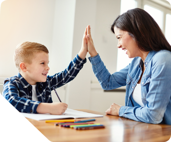 A female tutor sits with a young male student during a tutoring appointment. They are smiling and high fiving each other.