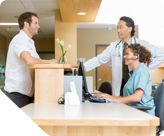 A male doctor talks to a male patient as he checks in at the receptionist's desk. the receptionist is looking at the patient and smiling.