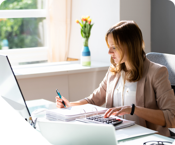 A woman accountant sitting at her desk writing and using a calculator.