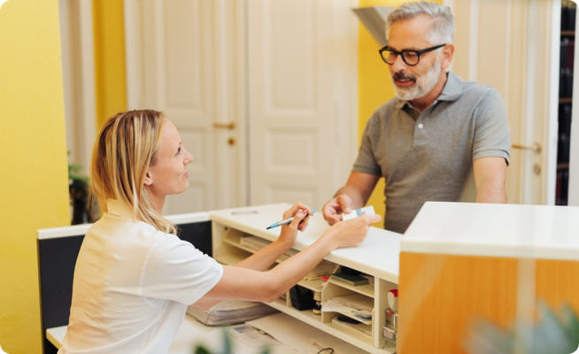 A female receptionist at a physical therapist's office checks in a male patient.