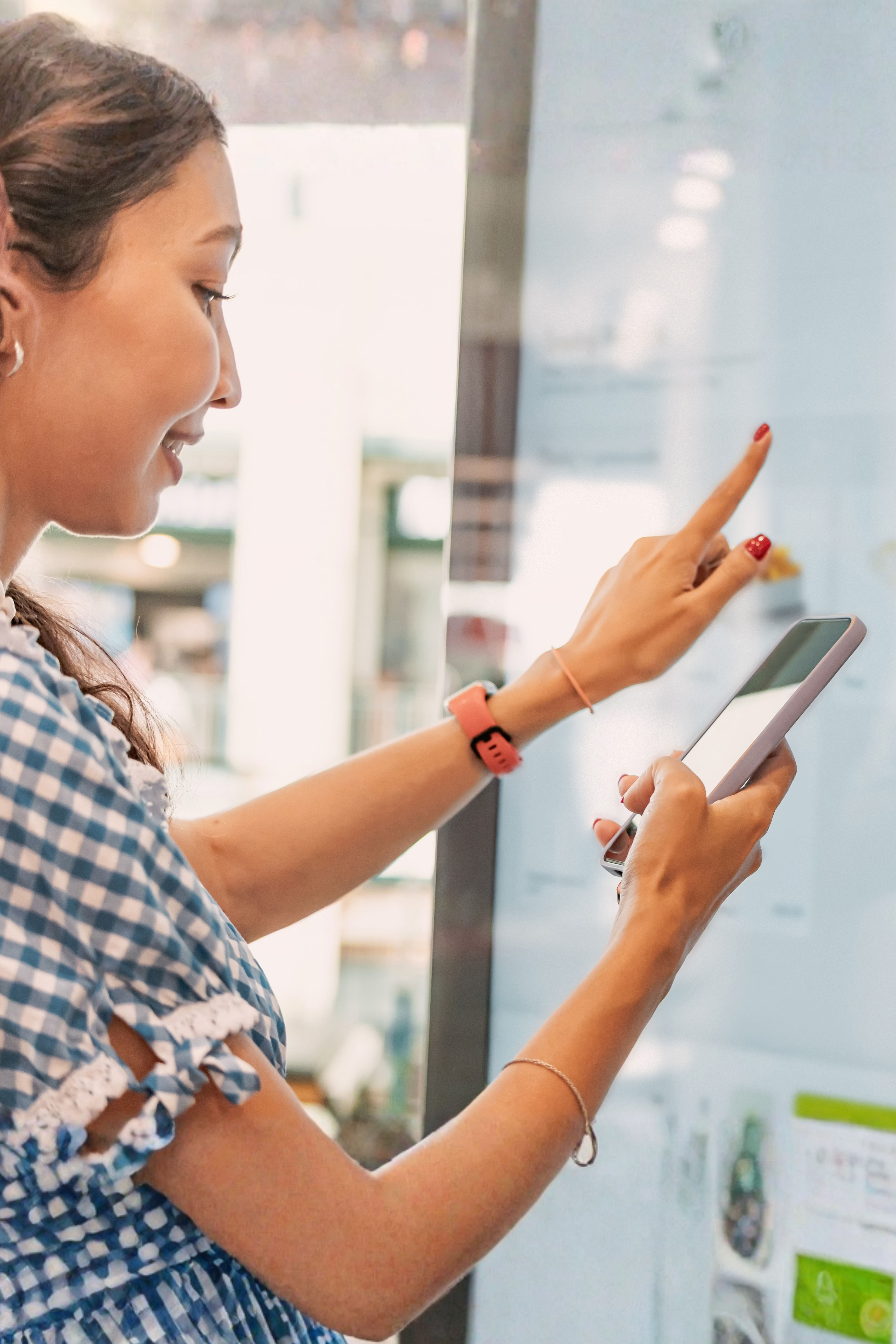 A woman in a checked shirt interacts with a touchscreen display while holding a smartphone