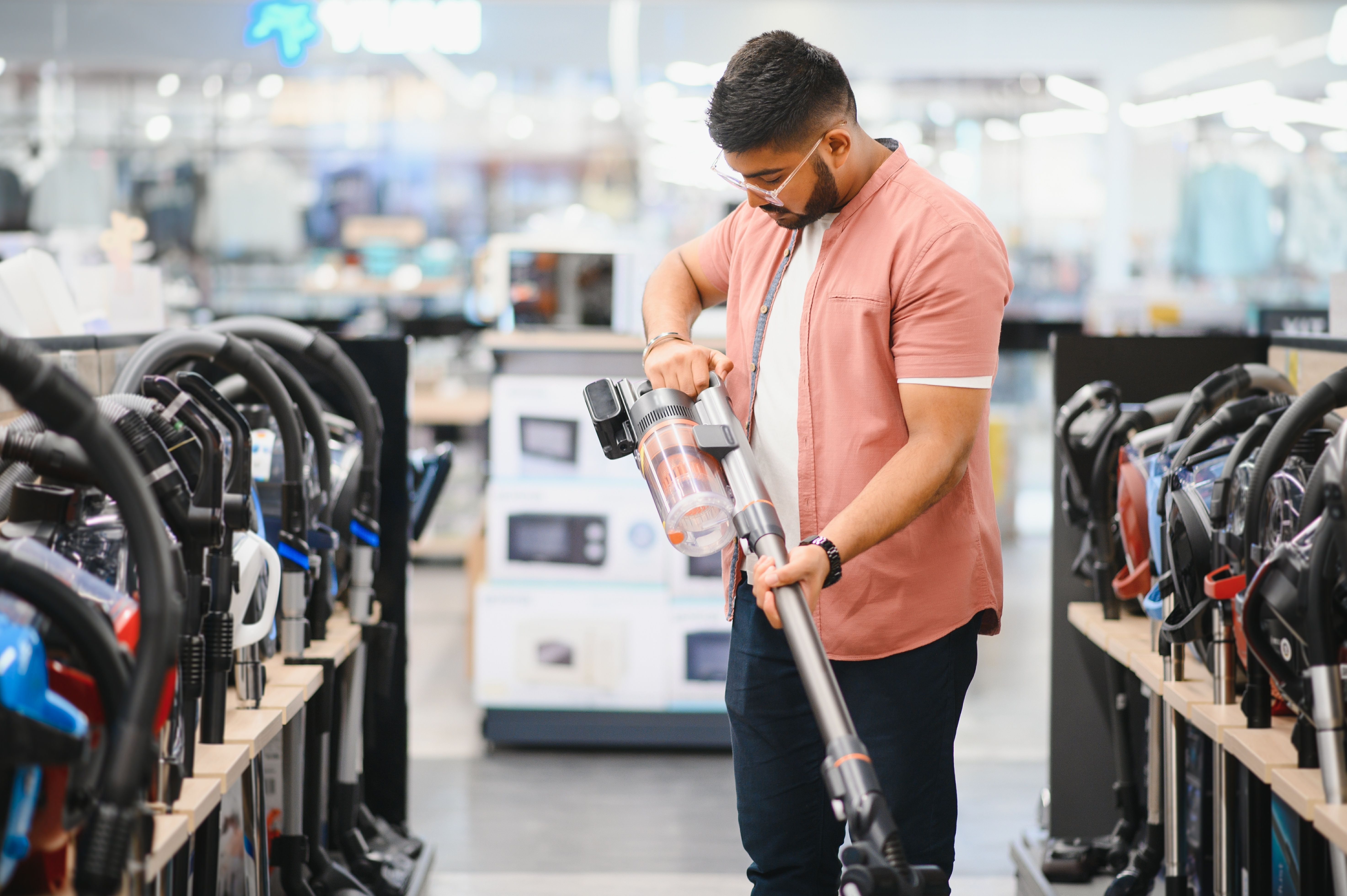 A man looking a handheld vacuum cleaner while shopping in an electronics store