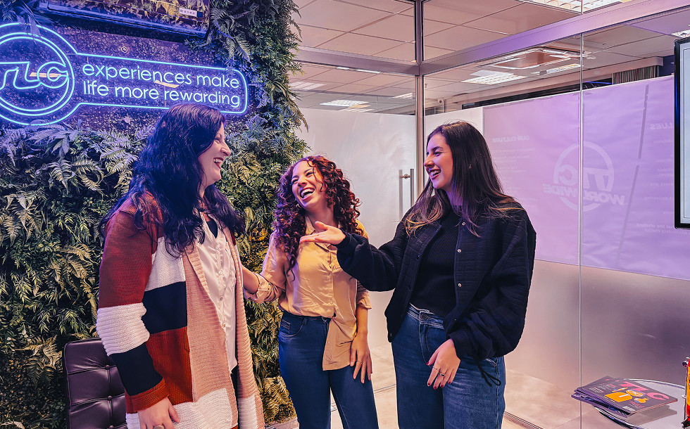 Three women chatting in front of a TLC logo and slogan