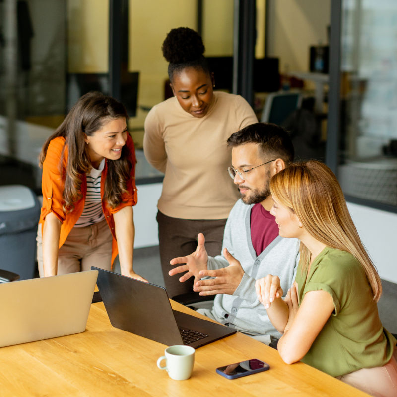 Two people sitting at a desk with a laptop explaining the results on the screen to two women standing