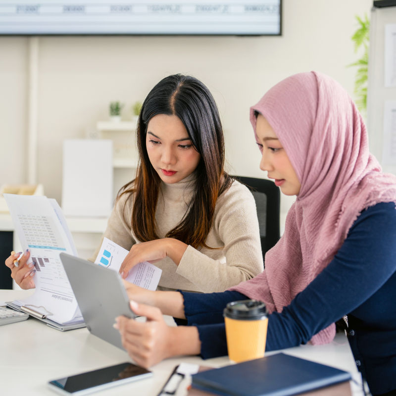 A woman with a laptop showing results to another woman who is looking at results on paper