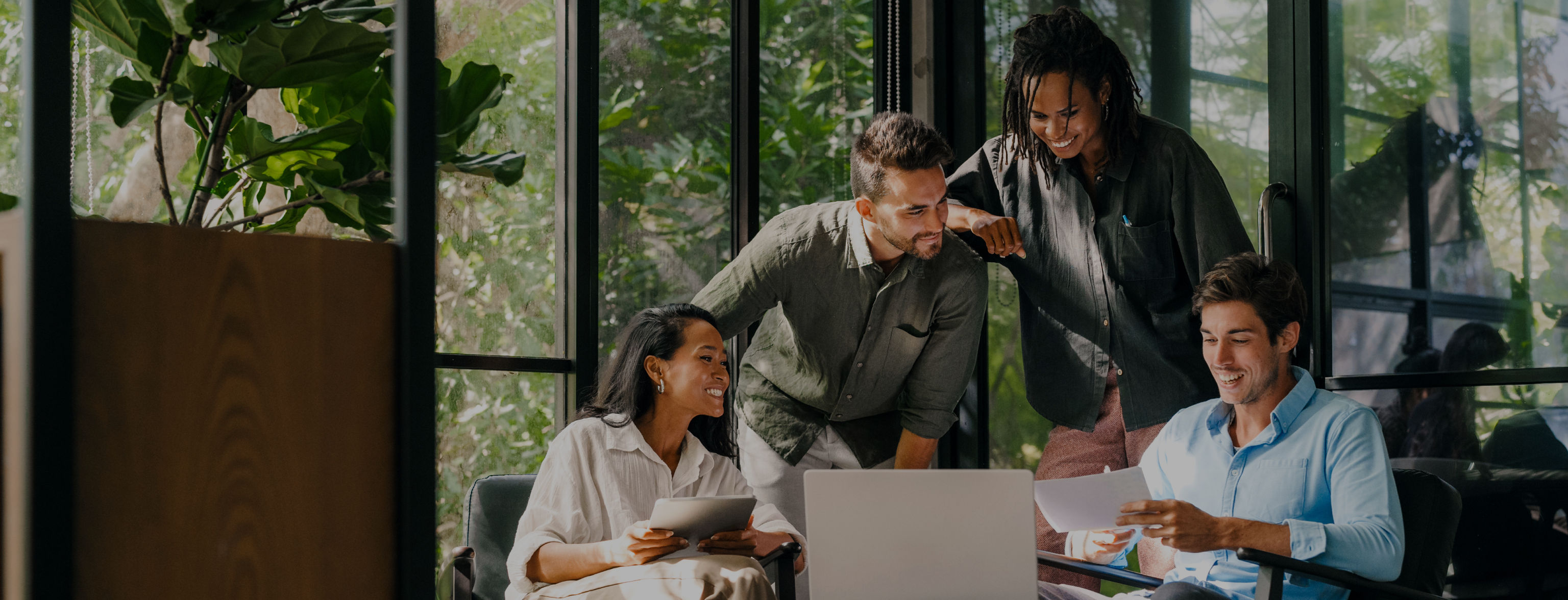 Two people sitting, two standing, facing a laptop and looking at a piece of paper